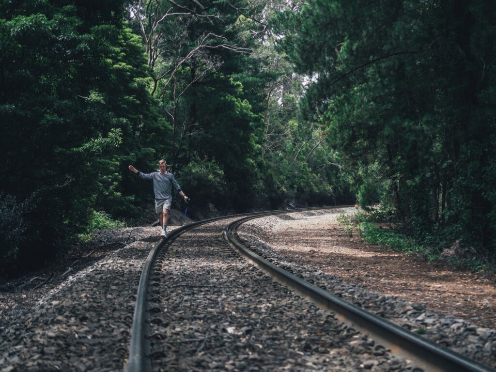 person walking through train rails between forest during daytime